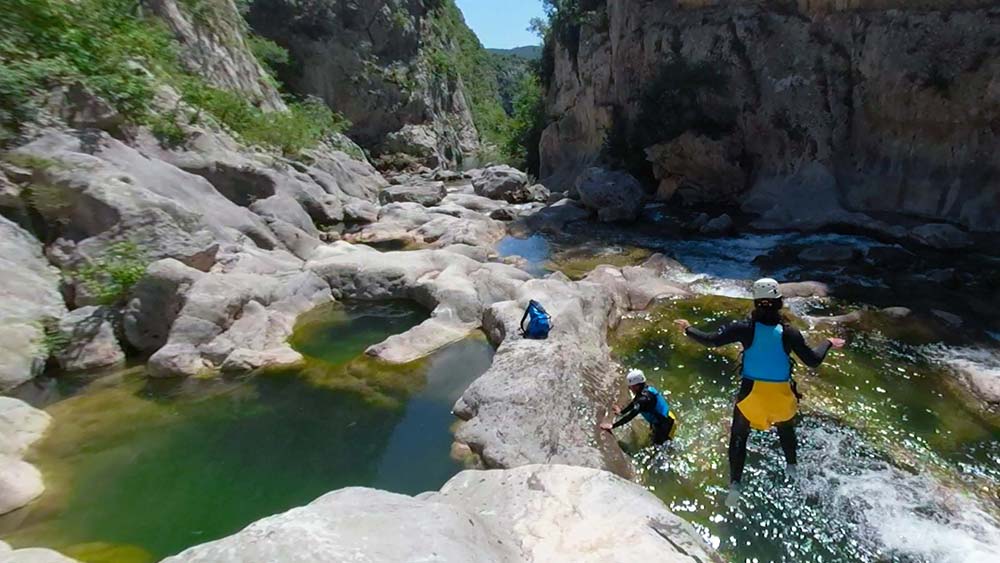 three people clambering on rocks in a river